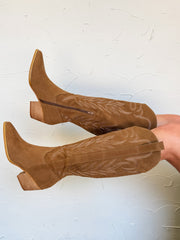 Brown cowboy boots worn by a person on a white background