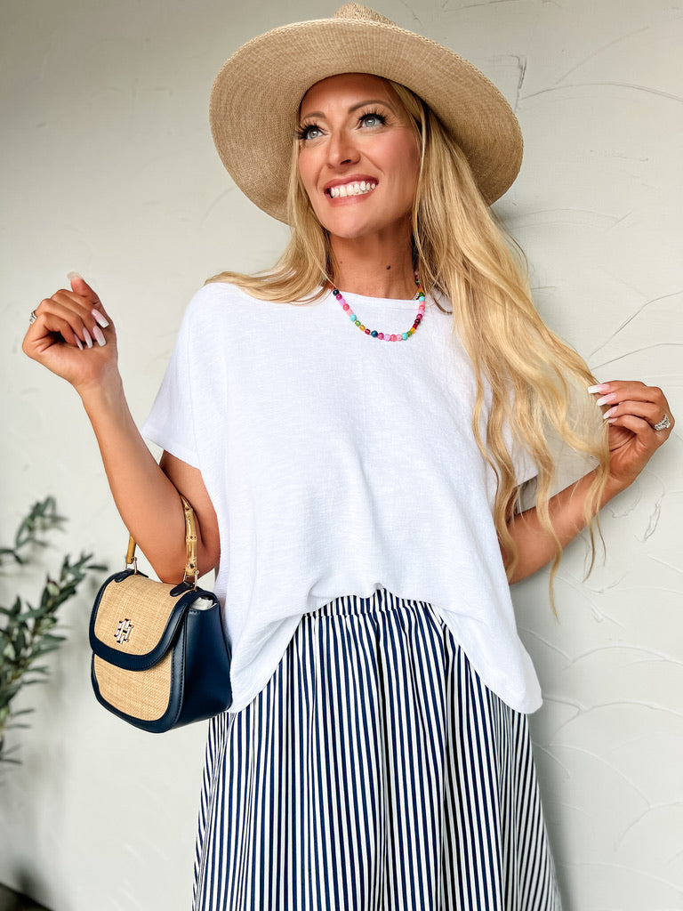 Woman wearing a white top, striped skirt, and straw hat with a handbag against a light background