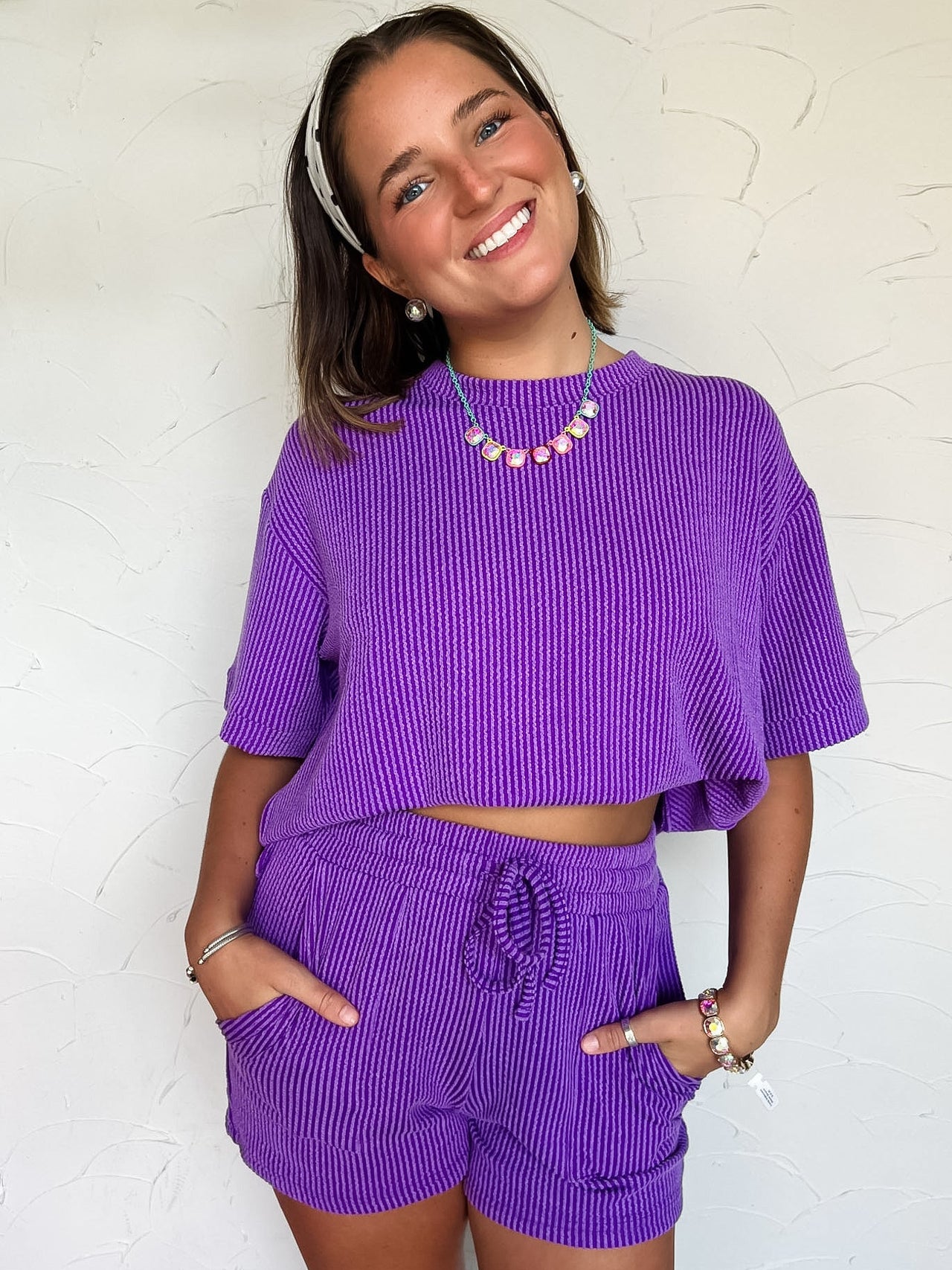 Woman wearing a purple set with a ribbed pattern against a white wall.