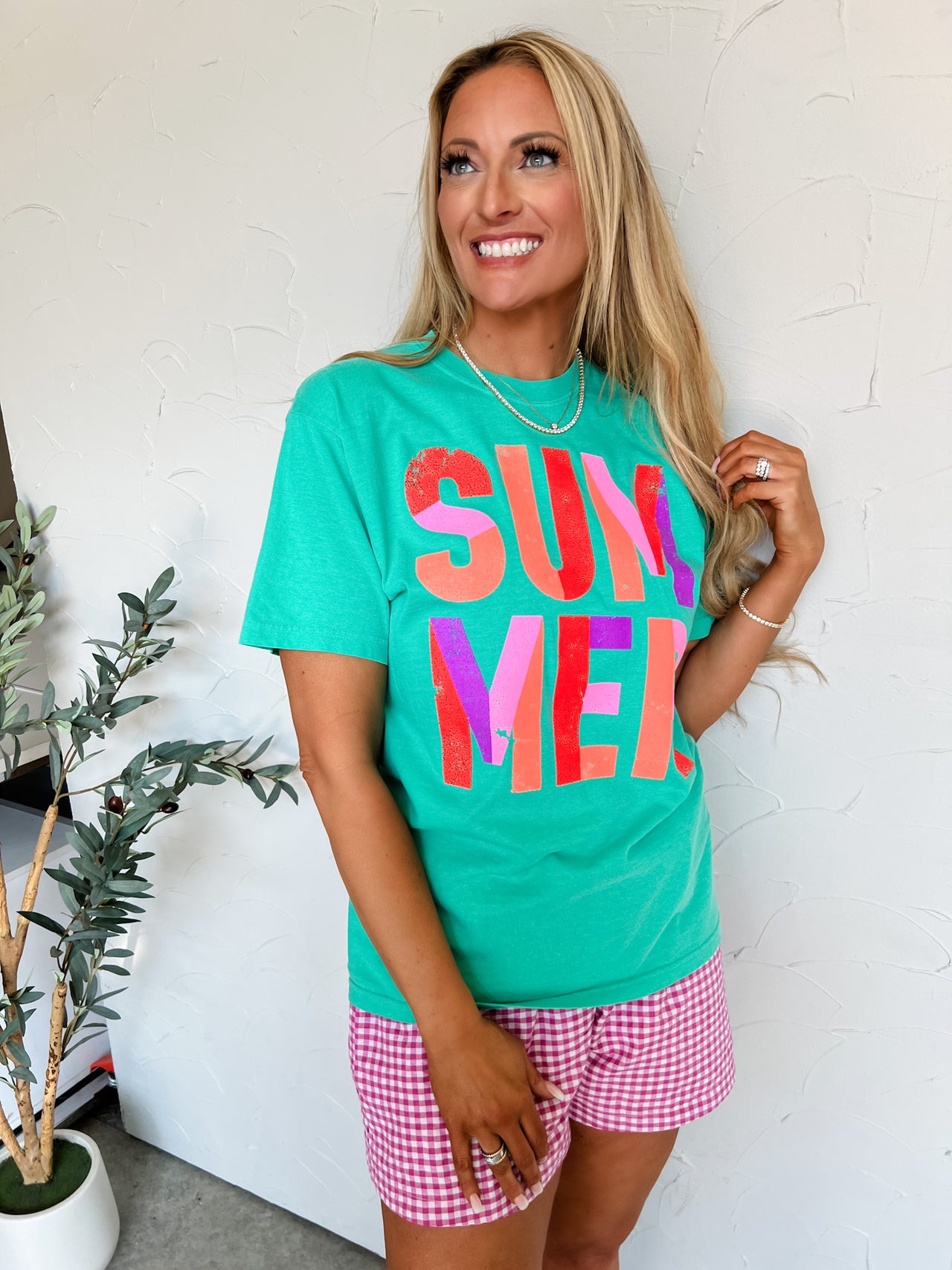 Woman wearing a green 'SUMMER' t-shirt and pink shorts indoors.