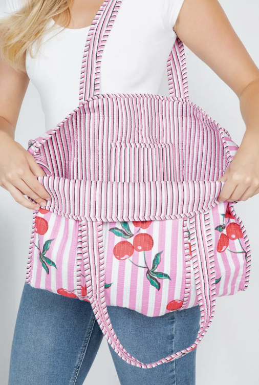 Person wearing a pink striped apron with cherry designs on a plain background