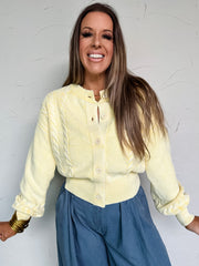 Woman wearing a yellow blouse and blue pants against a white wall