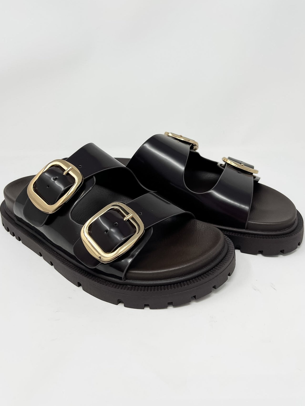 Dark brown sandals with gold buckles on a light gray background