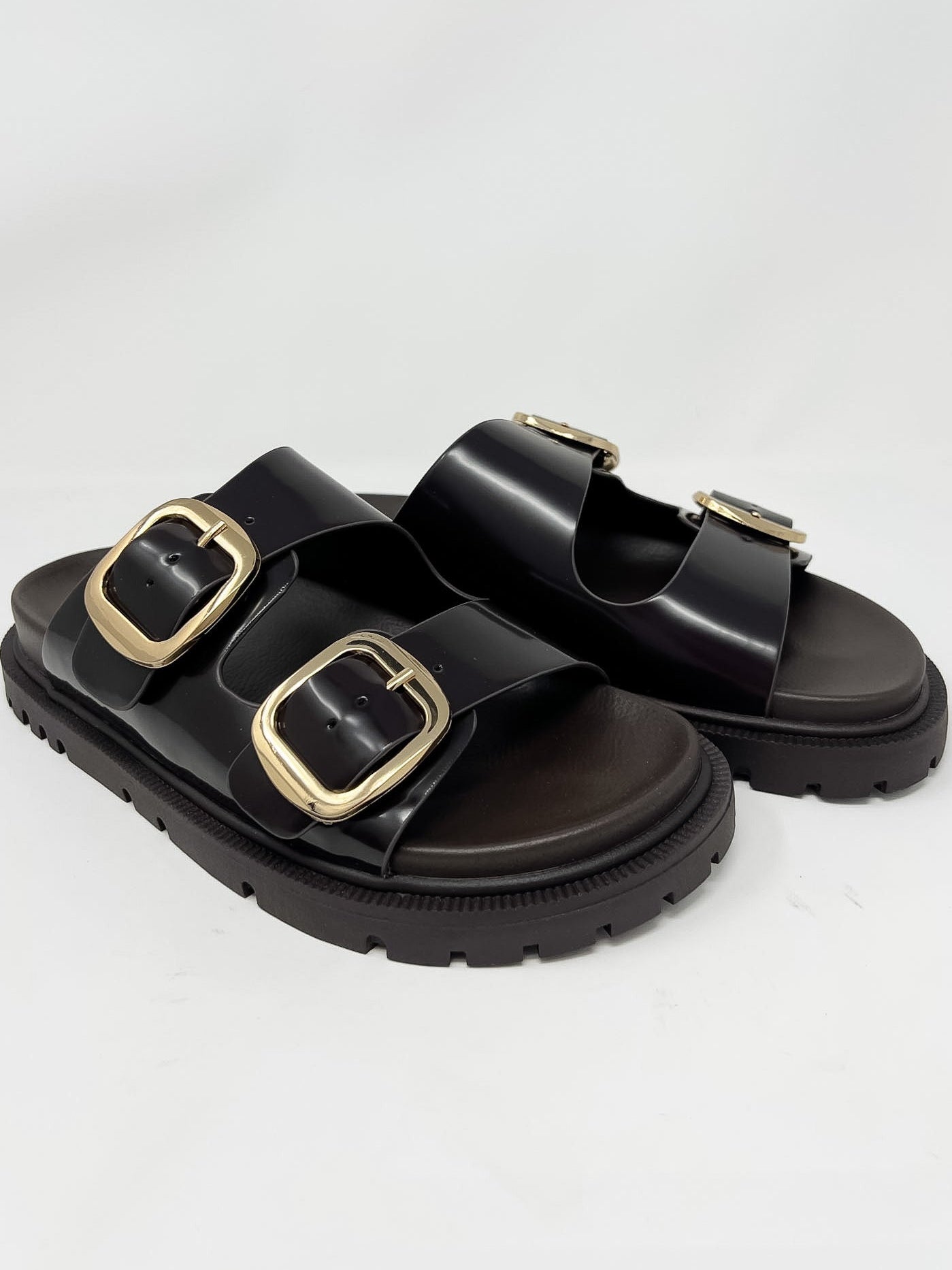 Dark brown sandals with gold buckles on a light gray background