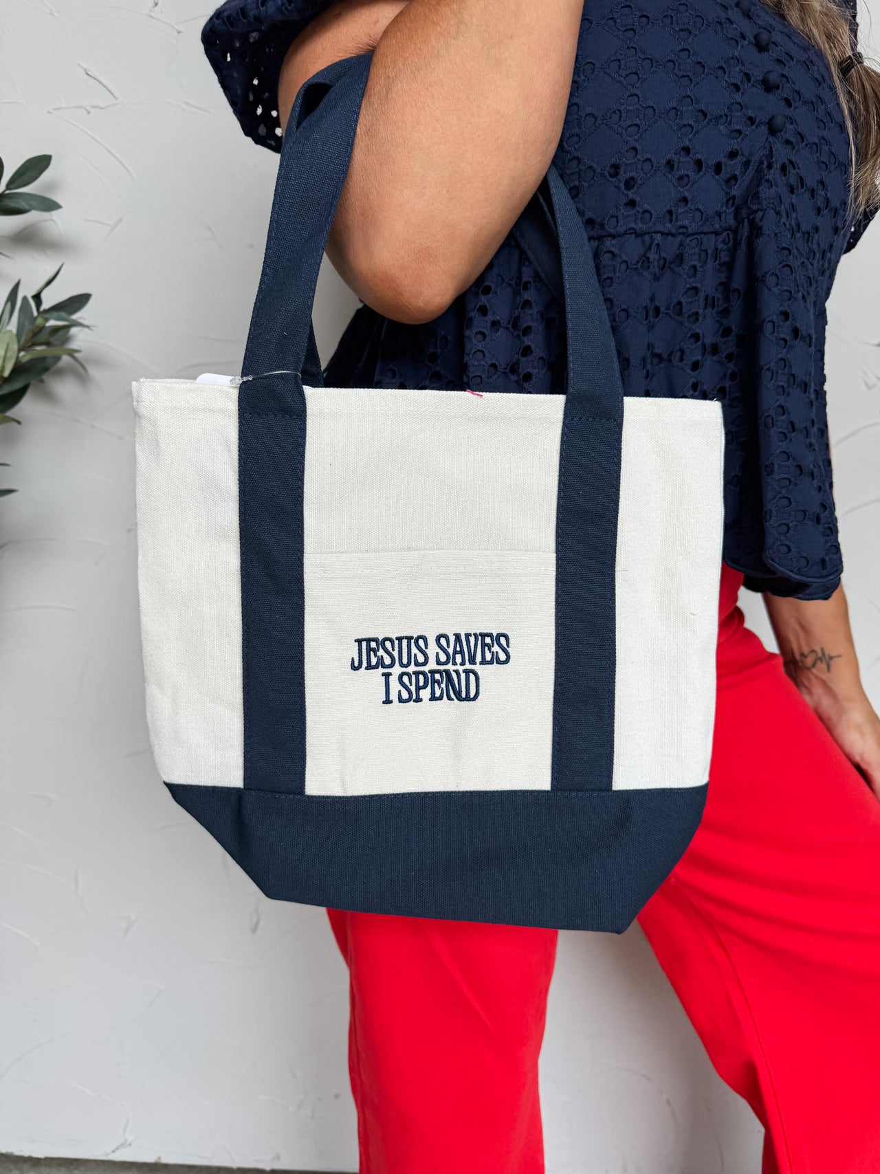 Person holding a tote bag with 'Jesus Saves I Spend' text against a white background