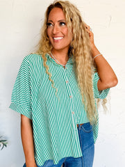 Woman wearing a green and white striped button up shirt and blue jeans against a white wall.