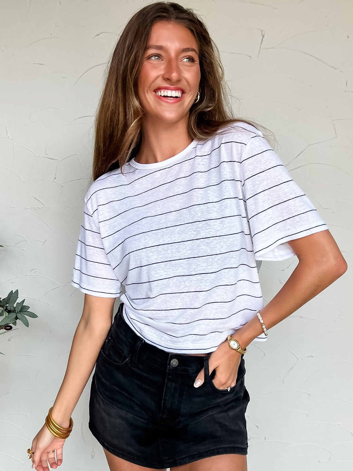 Woman wearing a striped shirt and black shorts standing against a white wall.
