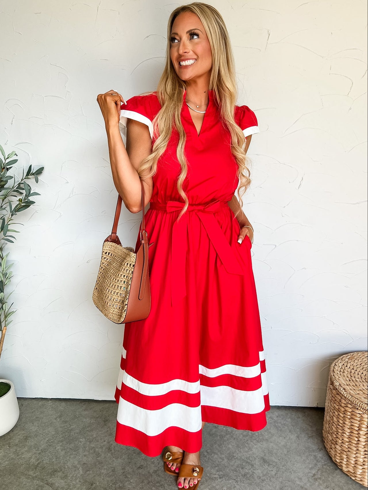 Woman in a red dress with white stripes standing against a white wall.