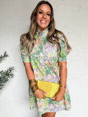 Woman wearing a floral dress with a yellow clutch against a white wall