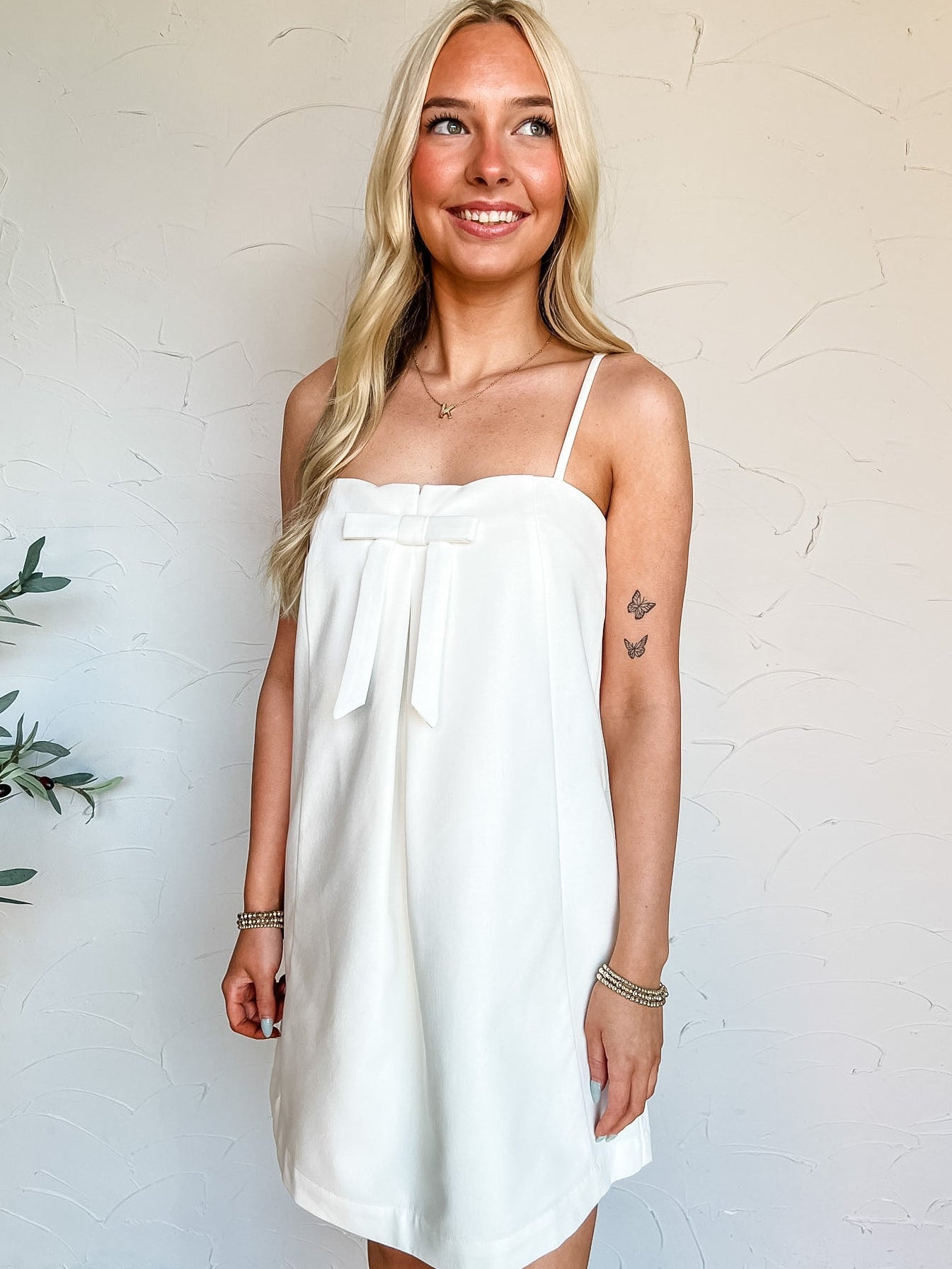 Woman wearing a white dress with a bow detail against a plain background
