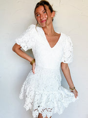 Woman wearing a white lace dress with bubble sleeves against a plain background