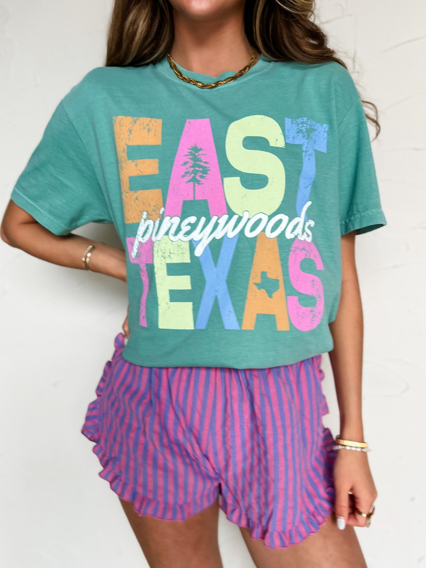 Person wearing a teal t-shirt with 'East Texas' text and purple striped shorts.