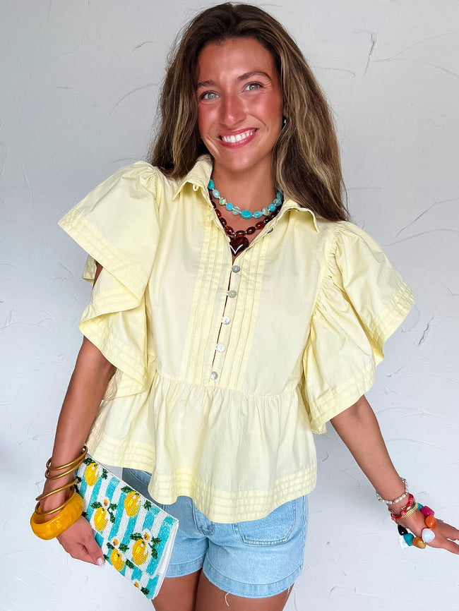 Woman wearing a yellow blouse and denim shorts, holding a colorful clutch against a white background