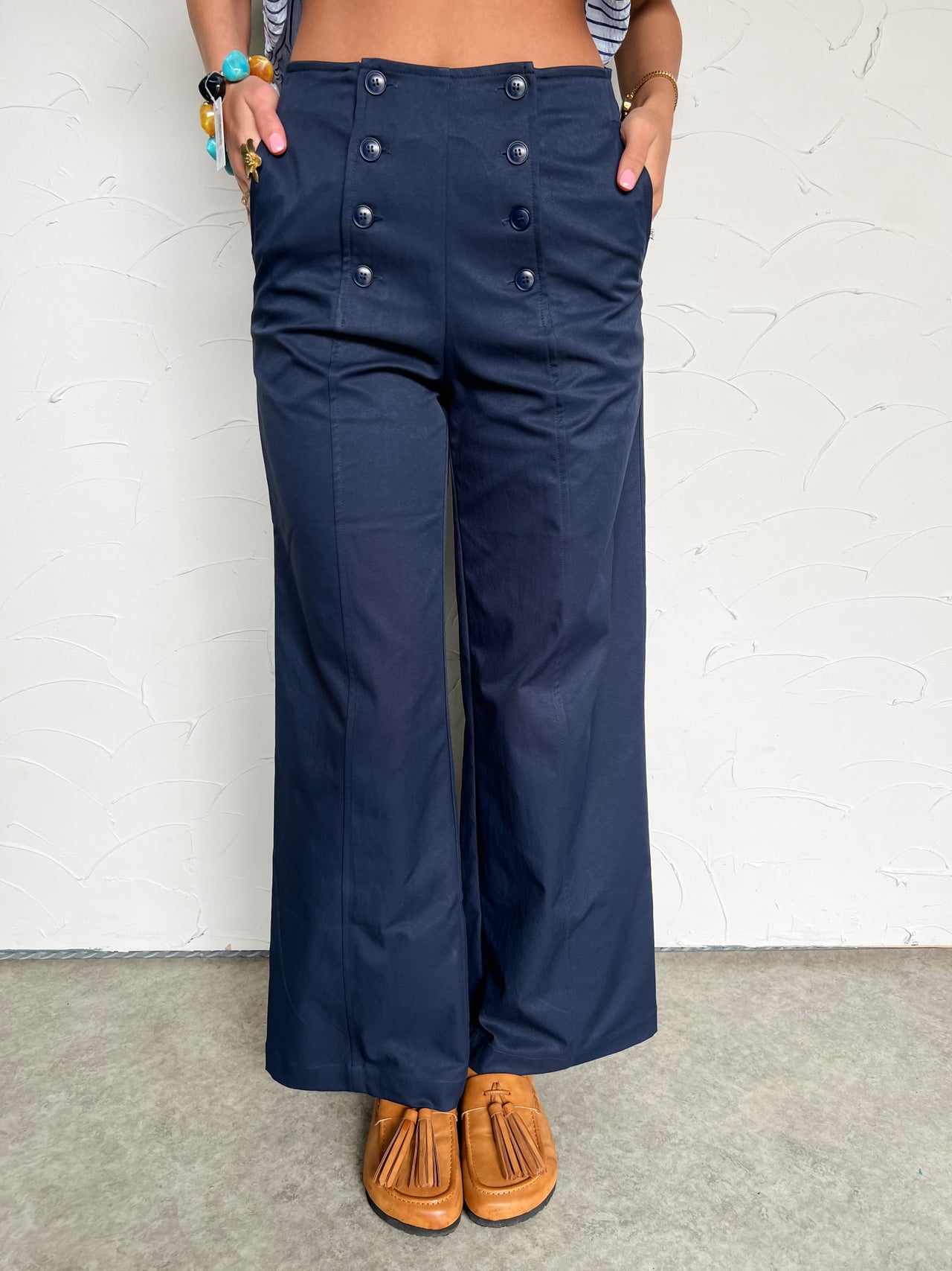 Person wearing navy blue wide-leg pants with button details against a white brick wall.