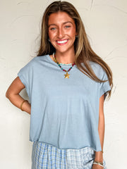 Woman wearing a light blue top and checkered shorts against a white wall