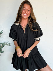 Woman wearing a black dress with white detail against a white wall
