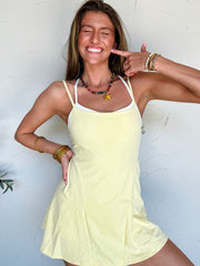 Woman wearing a yellow athletic dress with a built in white bra against a white wall