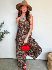 Woman wearing a leopard print romper with a red handbag and straw hat against a white wall.