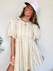 Woman wearing a short floral babydoll dress and cap with a white background