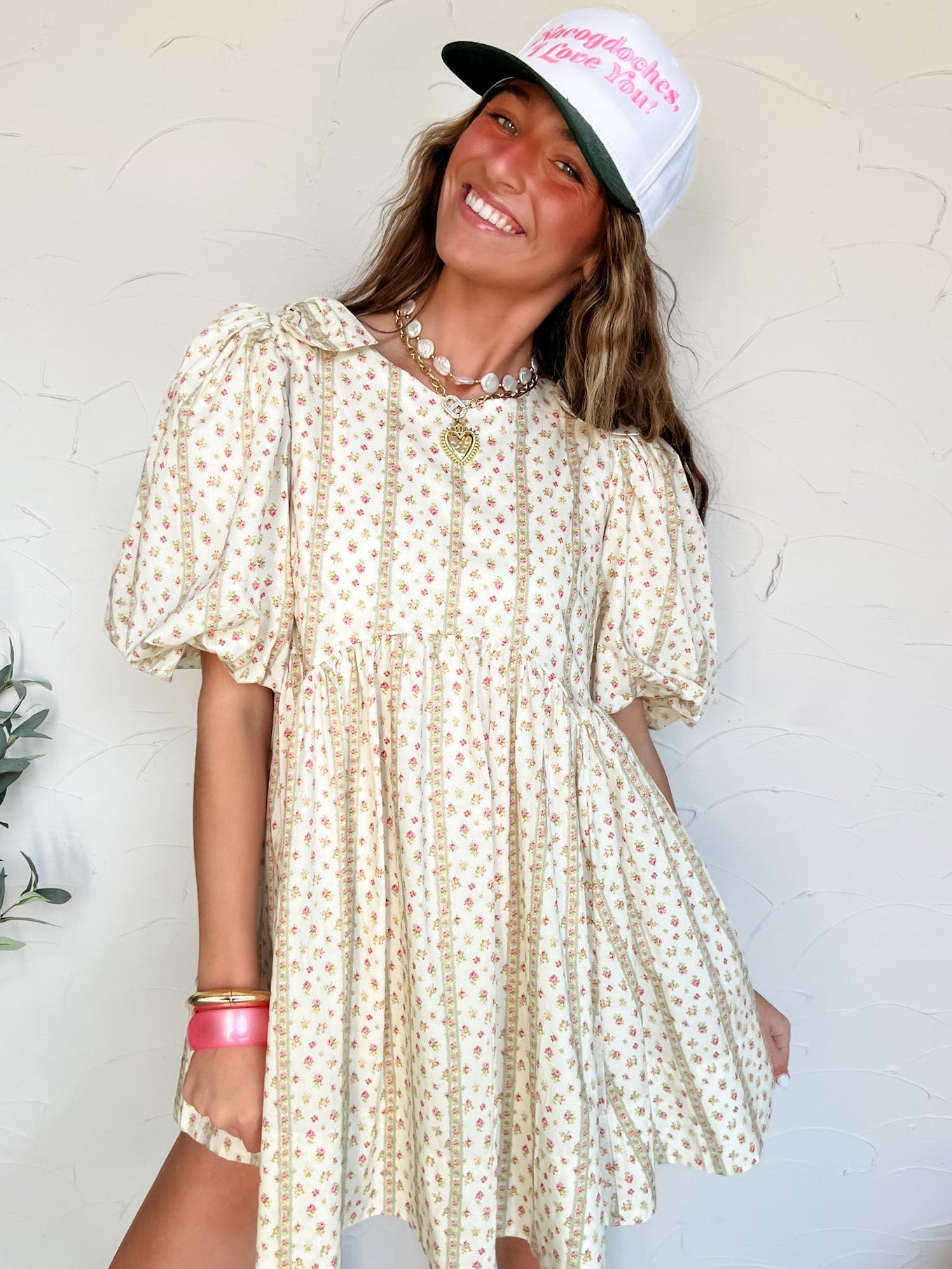 Woman wearing a short floral babydoll dress and cap with a white background