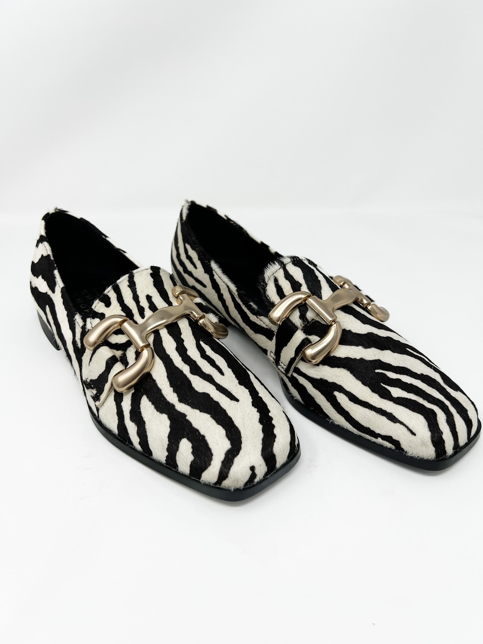 Pair of zebra print faux fur loafers with gold buckles on a white background