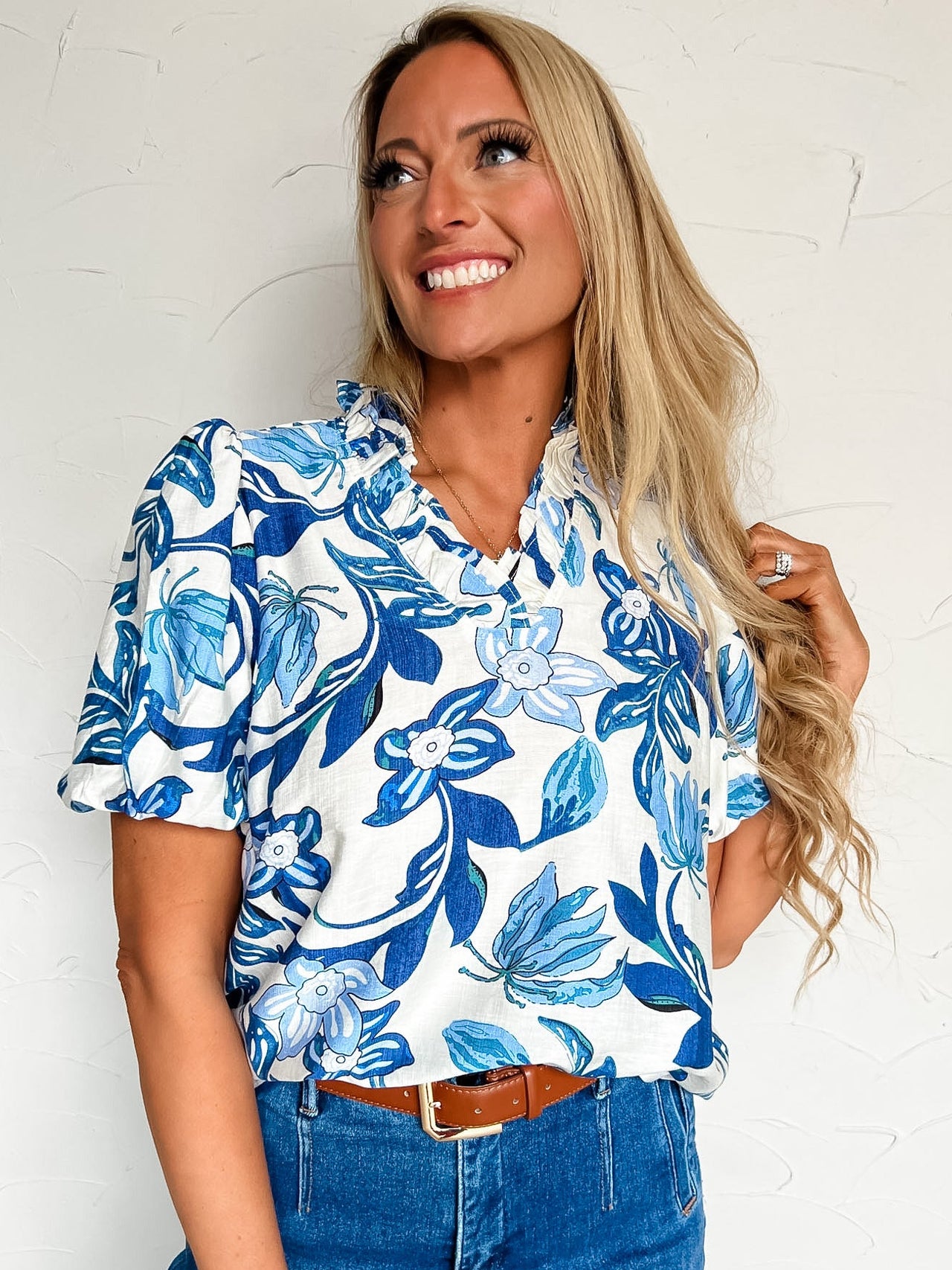 Woman wearing a blue floral blouse and jeans against a white background