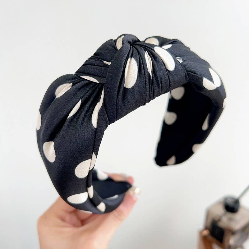 Black headband with white polka dots held by a hand against a light background