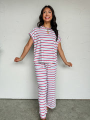 A two-piece casual lounge set featuring a multi-colored horizontal stripe pattern in red, blue, and light grey/white, crafted from a soft knit fabric blend of 95% cotton and 5% spandex. The set includes an oversized, relaxed-fit short-sleeve top with a matching patterned crew neckline and folded sleeve cuffs. The coordinating wide-leg pants feature a relaxed fit and an elasticized waistband with an adjustable drawstring.