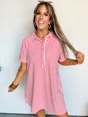 Woman wearing a red and white striped t-shirt dress against a white wall.