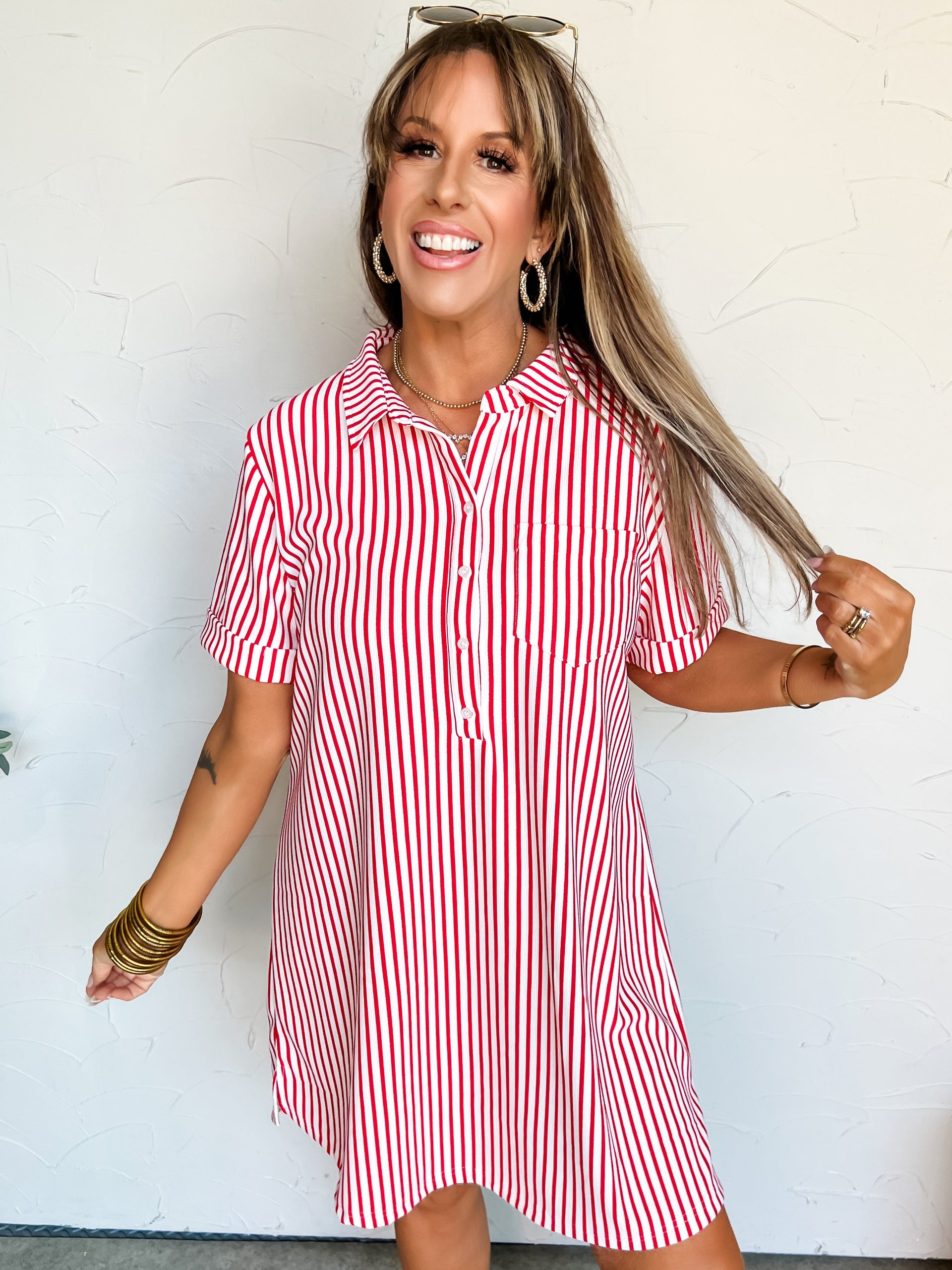 Woman wearing a red and white striped t-shirt dress against a white wall.