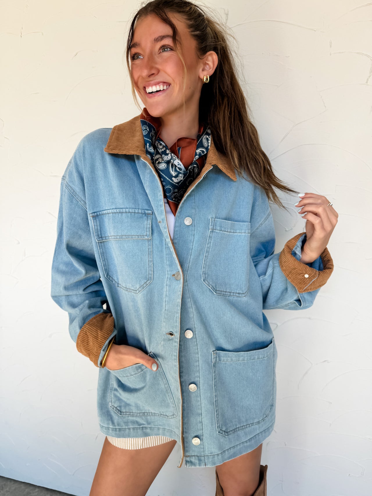 Woman wearing a denim jacket with brown corduroy collar and cuffs against a white wall