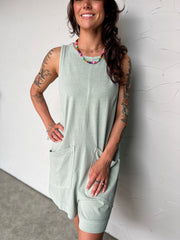 Woman wearing a light green sleeveless dress against a white wall.