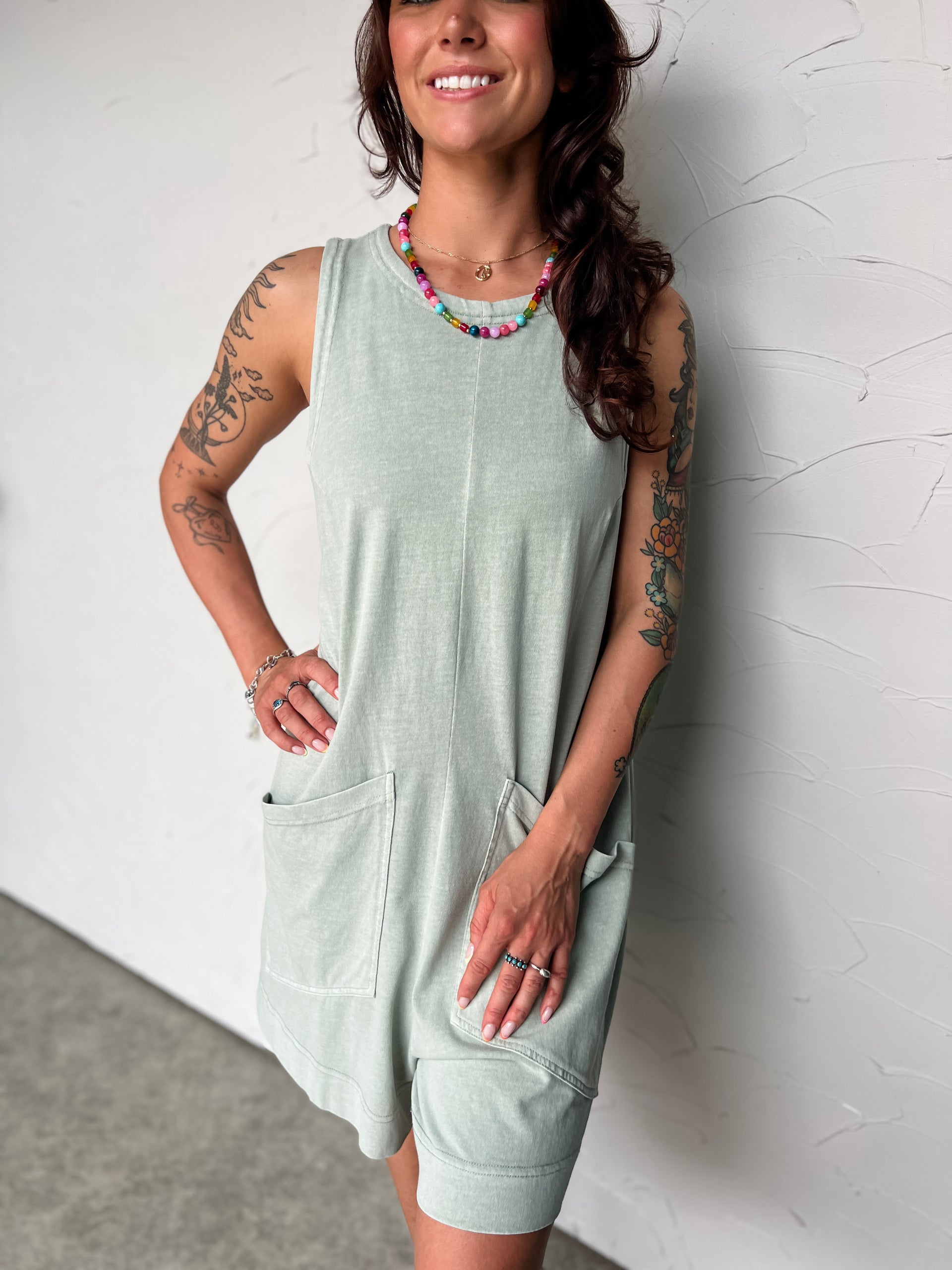 Woman wearing a light green sleeveless dress against a white wall.