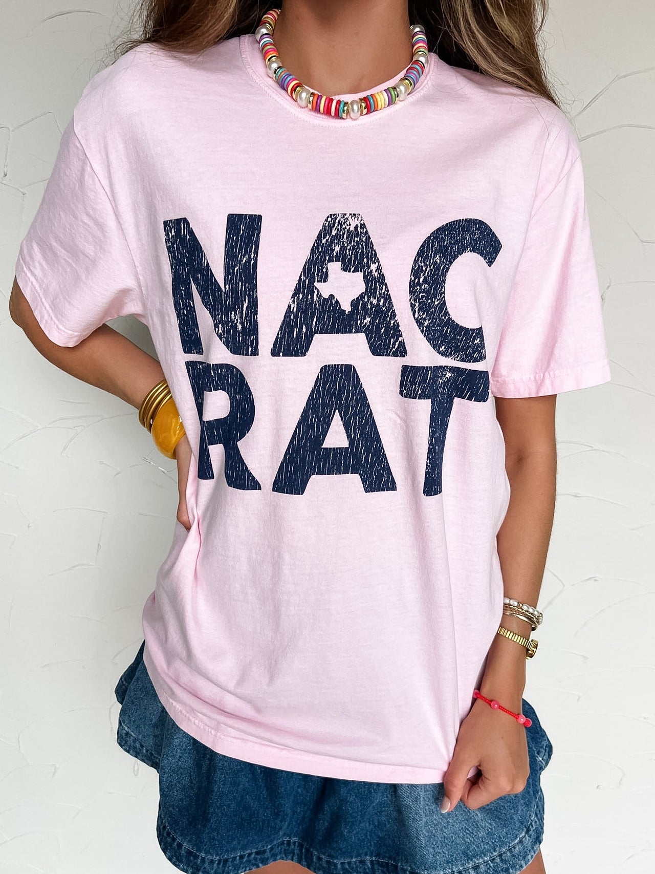 Person wearing a pink t-shirt with 'NAC RAT' printed on it against a white background