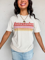 An off-white cream graphic tee shirt crafted from 100% cotton. The shirt features a classic crew neckline, short sleeves, and a relaxed fit, detailed with a distressed retro-style graphic across the chest that displays the text "Nacogdoches" in red lettering above a series of horizontal stripes in red, pink, orange, and yellow.