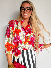 Woman wearing a colorful floral blouse and striped pants against a white wall.