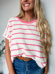 Woman wearing a white and pink striped top with blue jeans against a light background