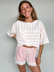 Woman wearing a pink and white striped top and shorts with lace trim against a light gray background