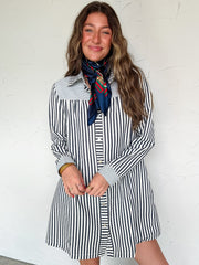 Woman wearing a black and white striped dress with a scarf, standing against a white wall.