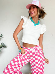 Woman wearing a white top, pink checkered pants, and a pink cap with a white background
