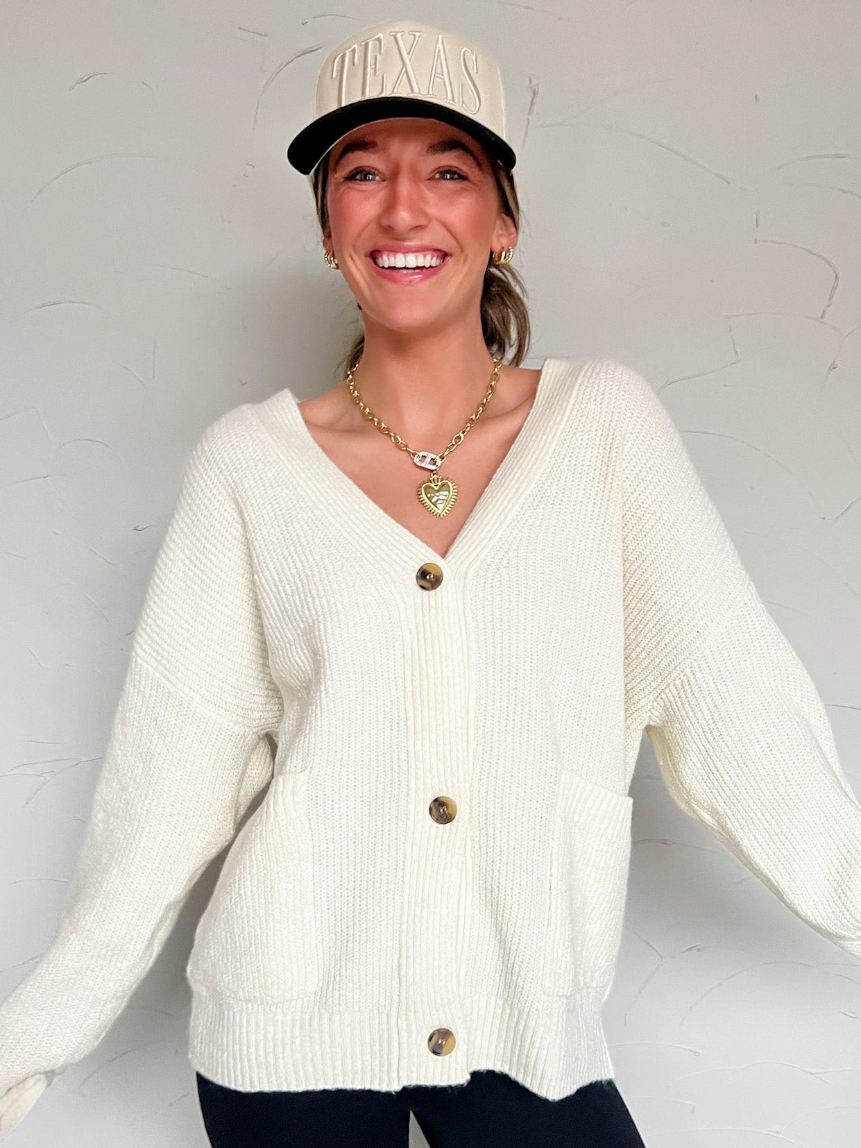 Woman wearing a cream cardigan and cream hat with black pants against a white background