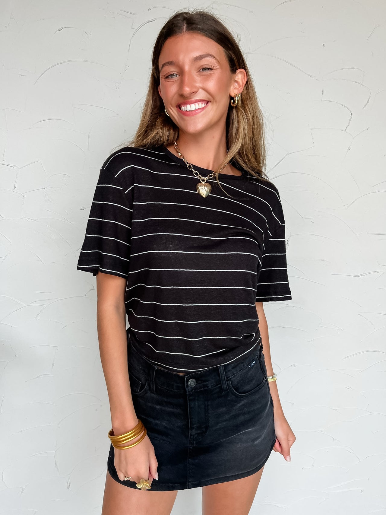Woman wearing a black and white striped shirt and denim Skort against a white wall.