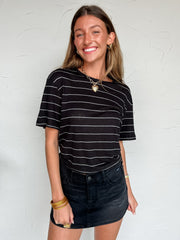 Woman wearing a black and white striped shirt and denim Skort against a white wall.