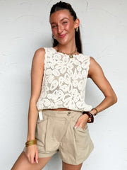 Woman wearing a white crochet top and beige shorts against a white wall.