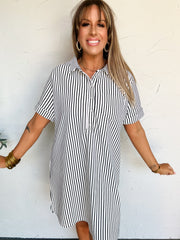 Woman wearing a black and white striped t-shirt dress against a white wall.
