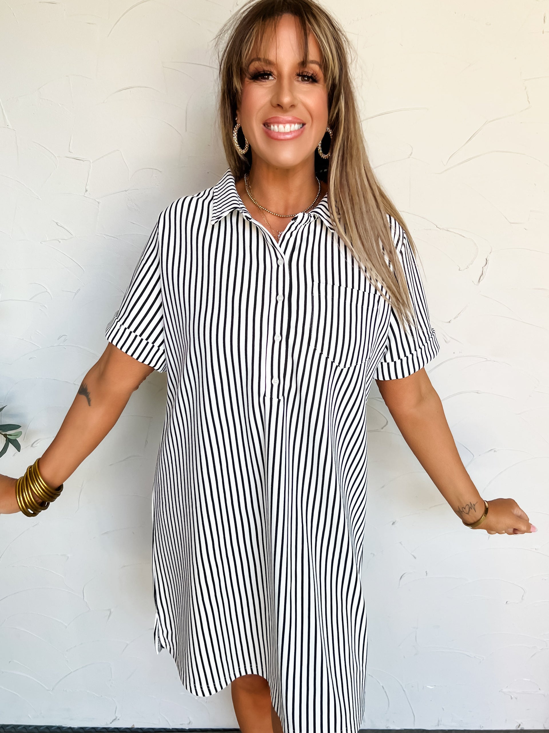 Woman wearing a black and white striped t-shirt dress against a white wall.