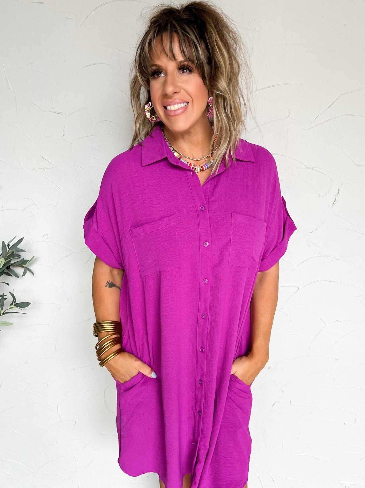 Woman wearing a purple shirt dress against a white wall.