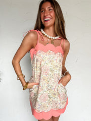 Woman wearing a floral dress with a coral scallop top and bottom against a white wall.