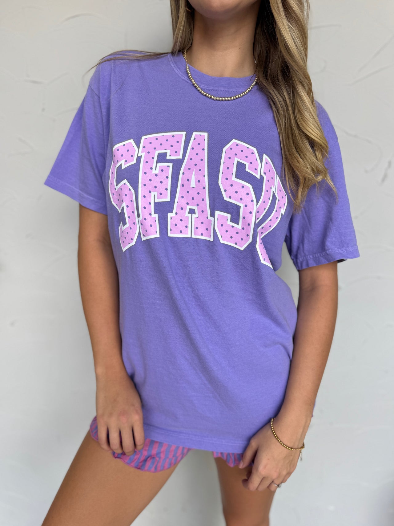 Person wearing a purple t-shirt with 'SFASU' printed on it against a white background