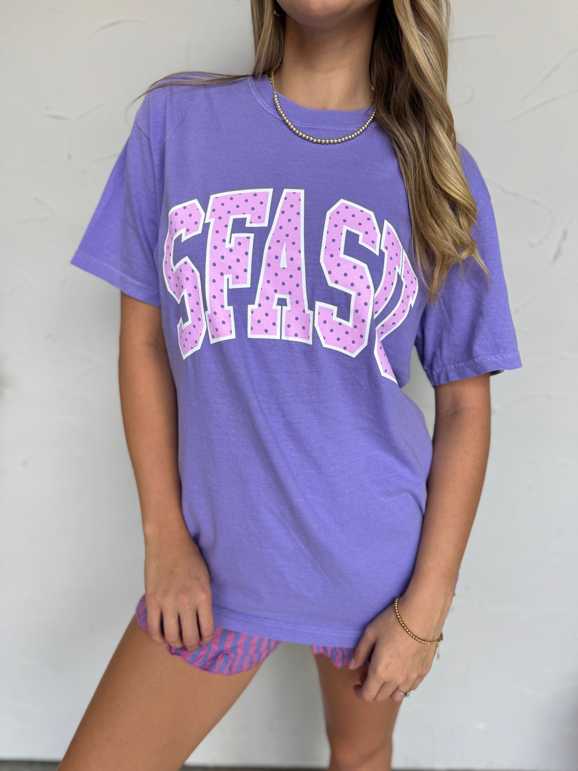 Person wearing a purple t-shirt with 'SFASU' printed on it against a white background